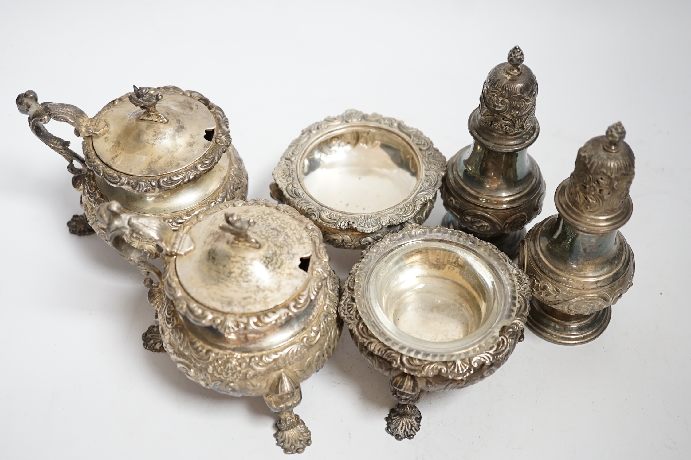 An ornate Edwardian silver four piece condiment set, with chinoiserie decoration by William Comyns, comprising two mustard pots and two salts, one with glass liner and a pair of similar pepperettes, all London, 1906, sal